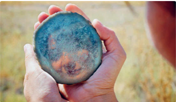 Mãos a segurar disco de obsidiana polida com reflexo.